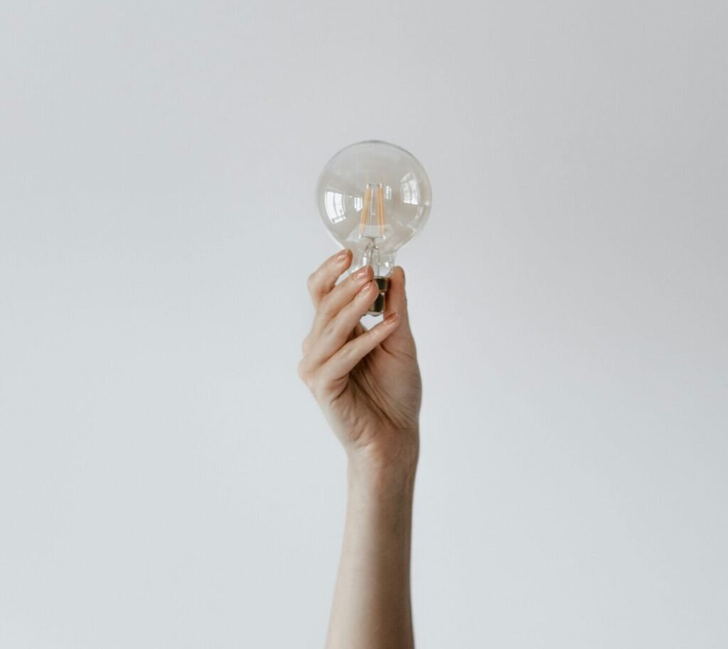 A hand raises a light bulb against a soft gray background, symbolizing creativity and ideas.